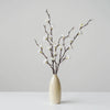A vase holds delicate artificial plum blossom branches with white flowers against a light gray background.