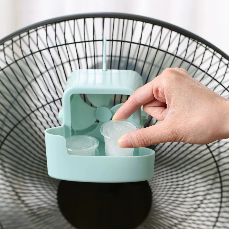 A hand is placing an ice cube into the compartment of a teal portable ice-cooling floor fan.