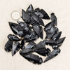 A collection of black obsidian arrow pendants scattered on a light fabric with a silver coin.