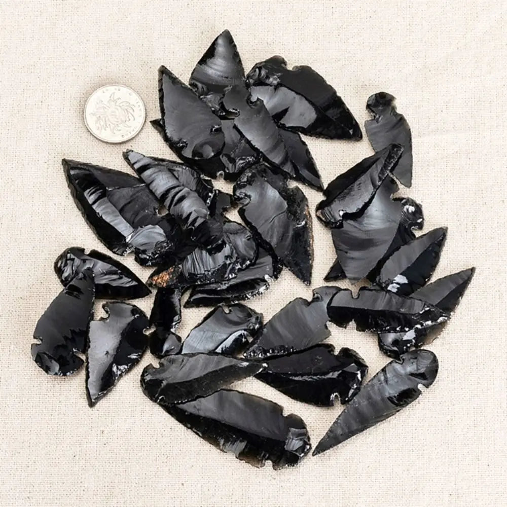 A collection of black obsidian arrow pendants scattered on a light fabric with a silver coin.