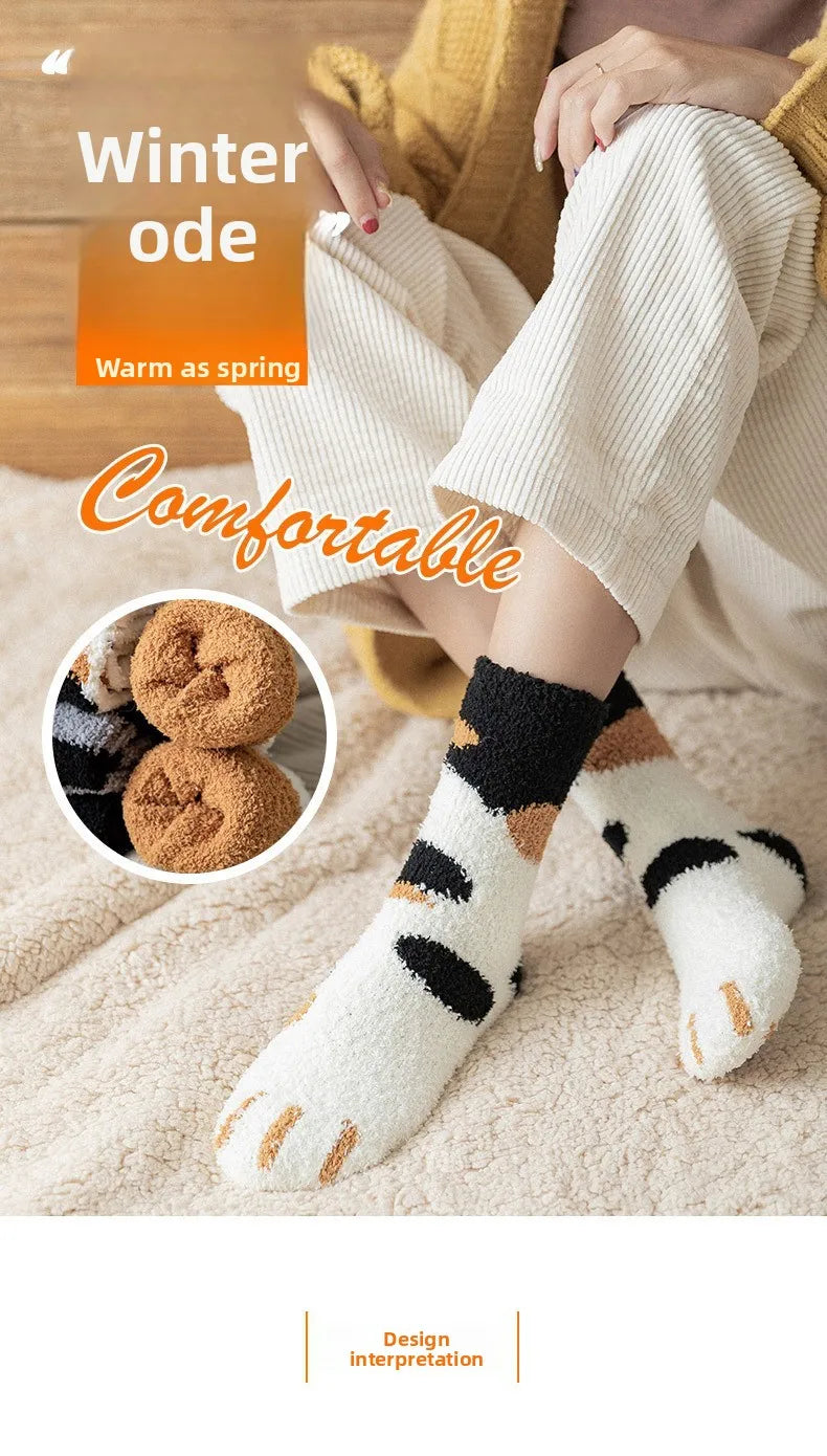 A close-up of a person wearing white plush socks with black and tan cat paw prints, paired with a yellow knit sweater.
