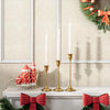 A set of three gold-toned metal candle holders with white taper candles displayed on a white mantelpiece.