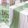 Sage green gauze table runner draped on a white tablecloth with silverware and wine glasses.