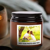 A dark brown jar candle with a black lid, featuring a photo of a couple embracing in a sunny outdoor setting.