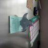 A silver 3D axe fridge magnet decorated with a calendar and various notes, used as kitchen decor.