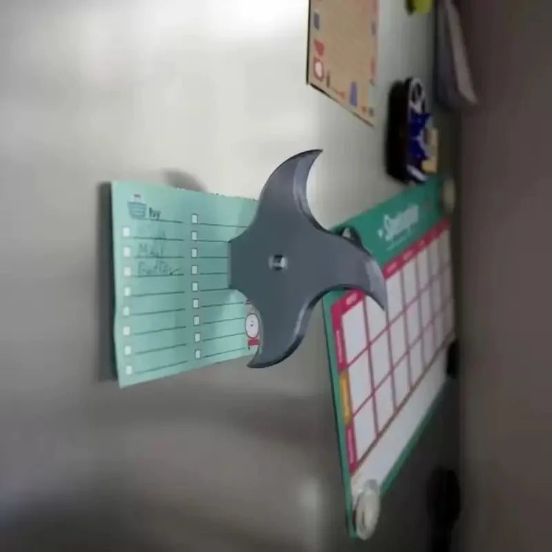 A silver 3D axe fridge magnet decorated with a calendar and various notes, used as kitchen decor.