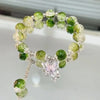 A bracelet made of small, round natural green and clear stones, featuring a silver charm shaped like a lily of the valley flo