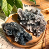 A pile of dark gray and clear natural zinc crystal clusters resting on a wooden surface with green leaves in the background.