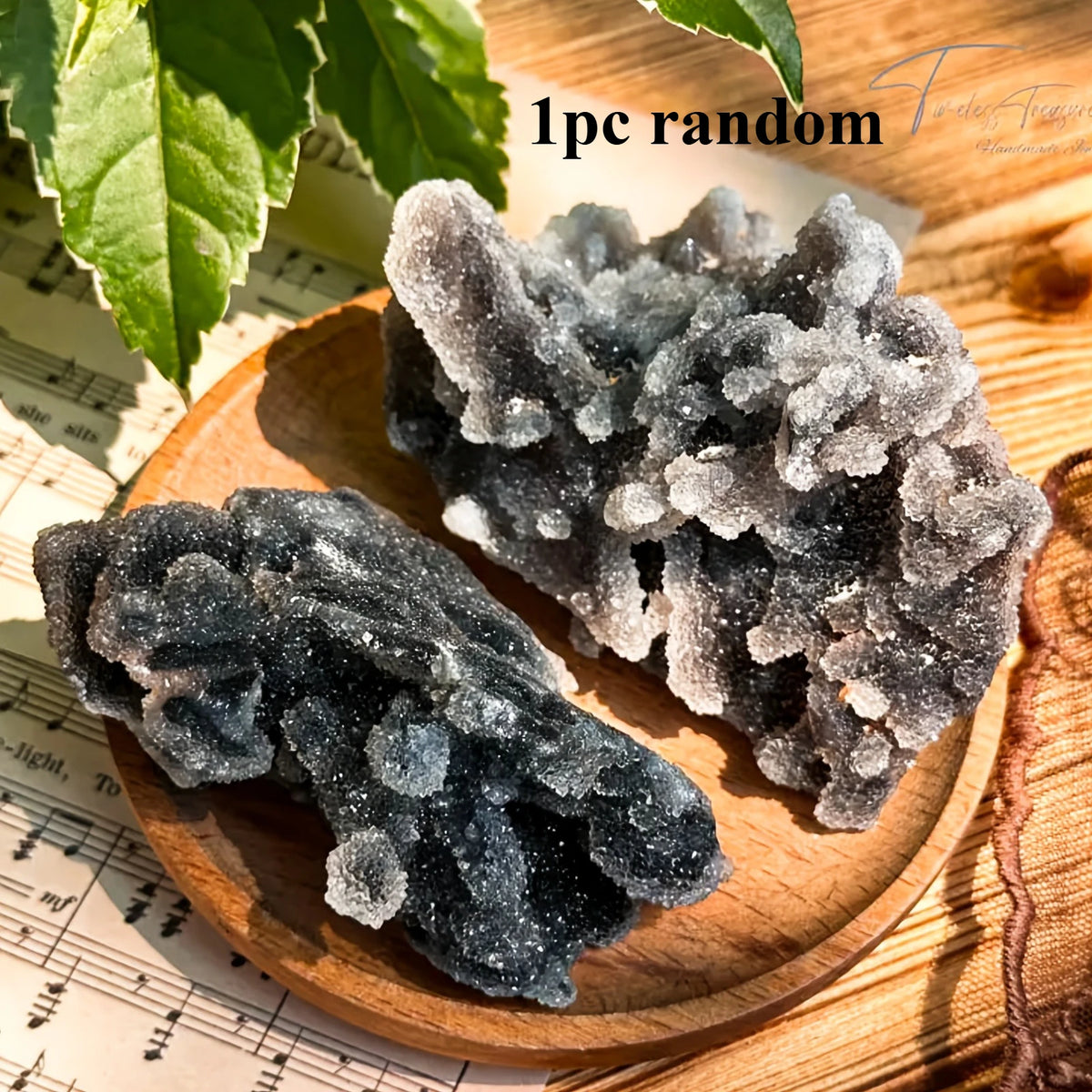 A pile of dark gray and clear natural zinc crystal clusters resting on a wooden surface with green leaves in the background.