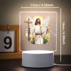 A glowing 3D LED night light featuring an angel with wings and a cross, set on a white base.