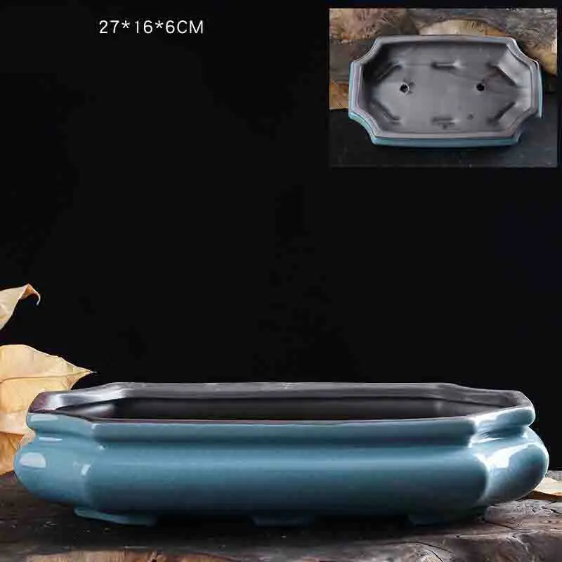 A blue glazed ceramic bonsai flower pot with a rectangular shape is shown on a dark surface.