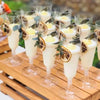 A set of disposable champagne glasses with a gold finish filled with a light yellow beverage and topped with a cream foam.