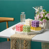 A display of white and pink cube soy wax candles arranged on a white platter with floral accents.