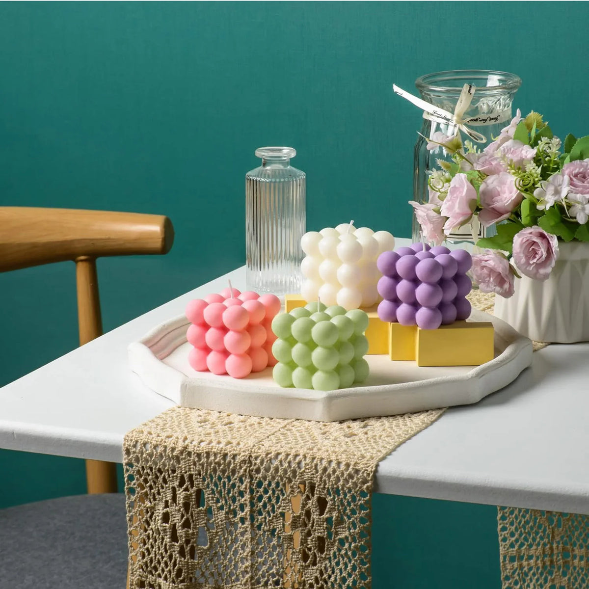 A display of white and pink cube soy wax candles arranged on a white platter with floral accents.