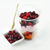A clear plastic cup filled with red cranberries and a slice of orange, next to a clear plastic lid.
