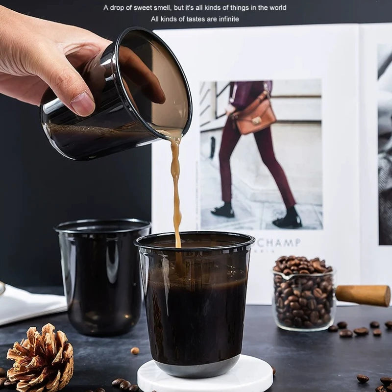 Eine Hand gießt eine dunkle Flüssigkeit aus einer Tasse in eine andere, vor einem Hintergrund mit Kaffeebohnen und einer Kief