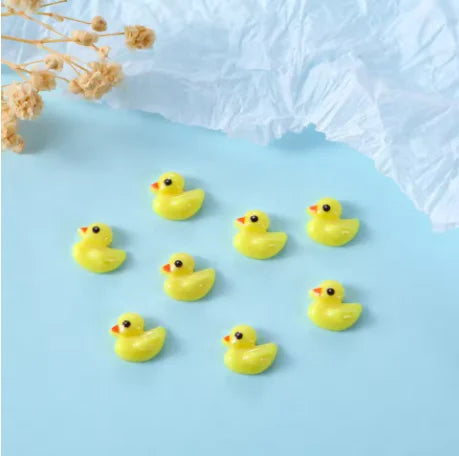 Una colección de 10 charms de uñas de tortuga amarilla esparcidos sobre un fondo azul claro.
