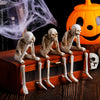 A set of three white resin skeleton skull figurines are displayed on a wooden box next to a carved orange jack-o'-lantern.