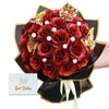A bouquet of deep red glitter roses with gold accents and pearl details presented in a dark brown paper wrapper.