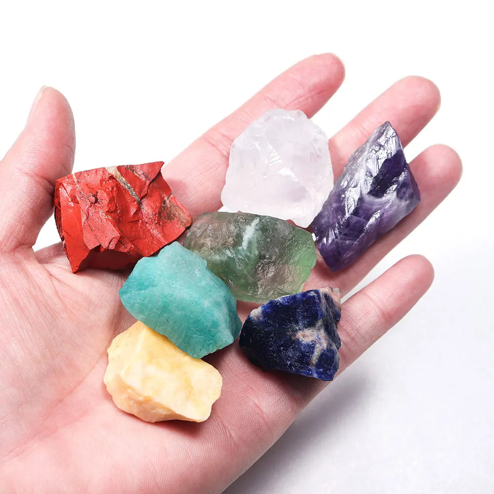 A hand holds a set of natural crystal healing stones in various colors including red, green, purple, and clear pink.