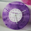 A purple vinyl record wall clock with a transparent cover and white face displaying midnight.