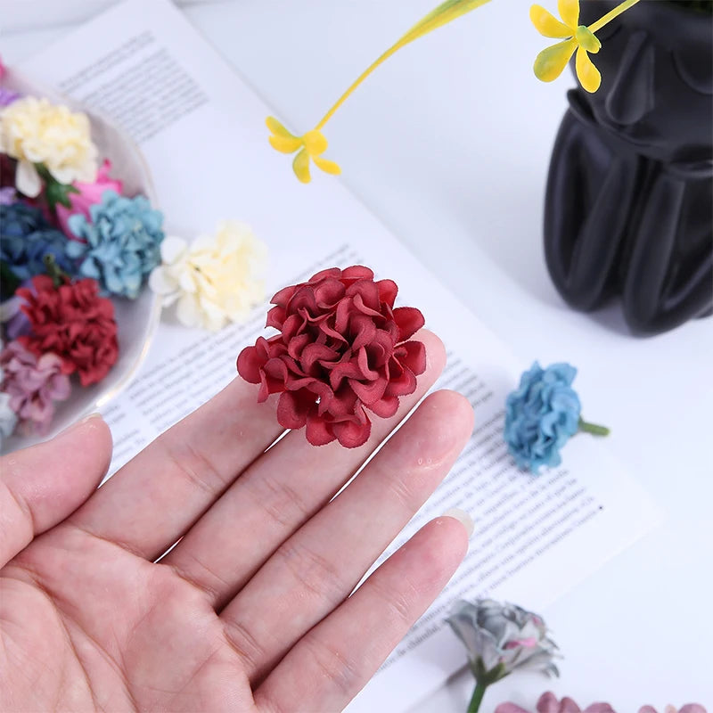 Une main tient un bouquet de petites fleurs artificielles en hydrangee rouge foncé à côté d'une feuille de papier et de fleur