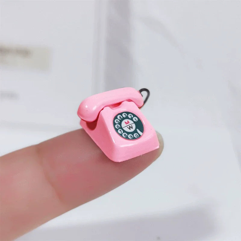 A pink vintage rotary desk phone miniature decor is held by a finger against a white background.