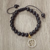 A handmade beaded bracelet featuring natural black stones and a gold zodiac charm.
