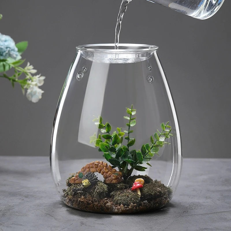 A clear glass vase filled with moss and small plants, being watered by a stream of water.