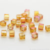 A collection of square cut glass crystal beads in shades of yellow and pink scattered on a white surface.