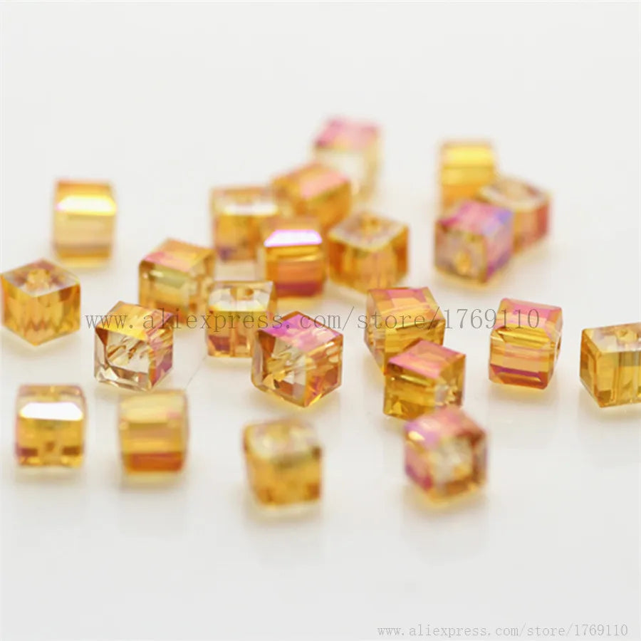 A collection of square cut glass crystal beads in shades of yellow and pink scattered on a white surface.