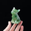 A small, translucent green crystal statue of a dog is held in a hand against a black background.