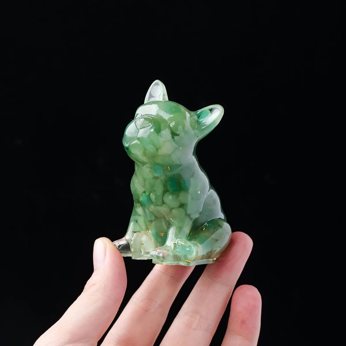 A small, translucent green crystal statue of a dog is held in a hand against a black background.