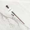 A black metal magic wand replica with a metallic core is displayed on a white marble surface.