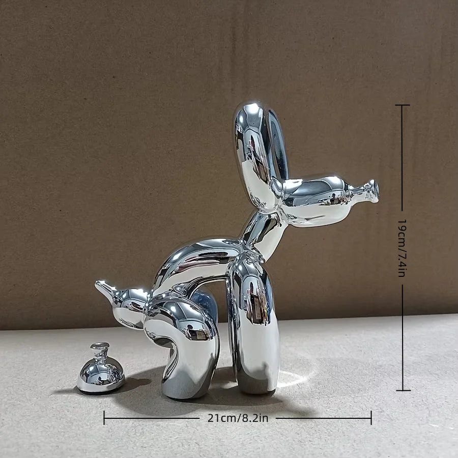 A silver metal sculpture of a dog in a squatting pose, displayed against a neutral background.