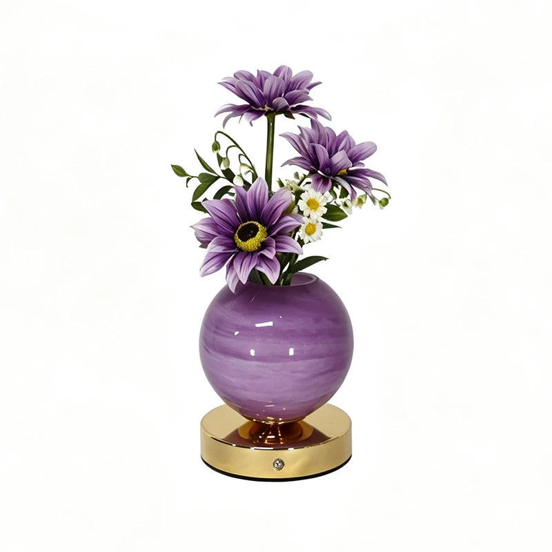 A purple glass vase holding purple and white flowers, resting on a gold base.