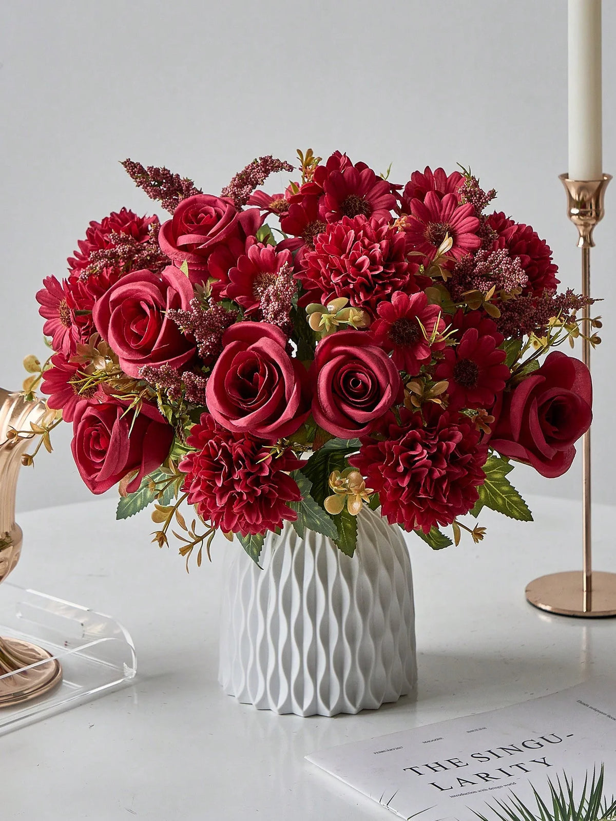 A vibrant bouquet of deep red and burgundy artificial silk flowers arranged in a white textured vase.