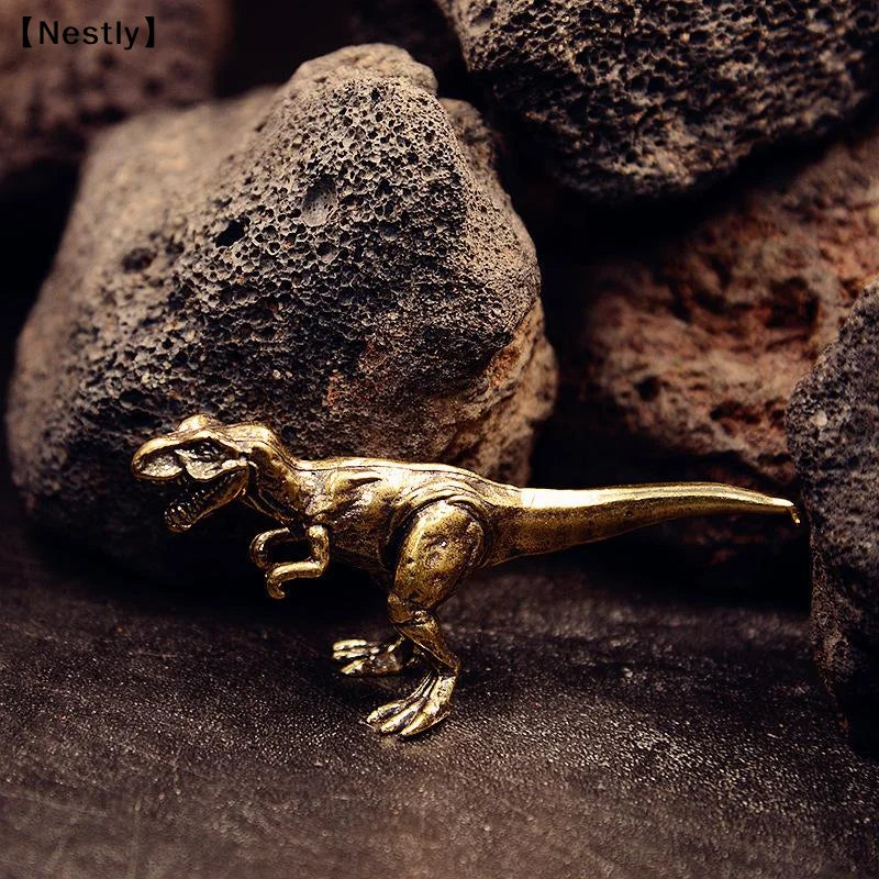 Un petit ornement de dinosaure en laiton solide posé sur une surface sombre parmi des rochers rugueux.
