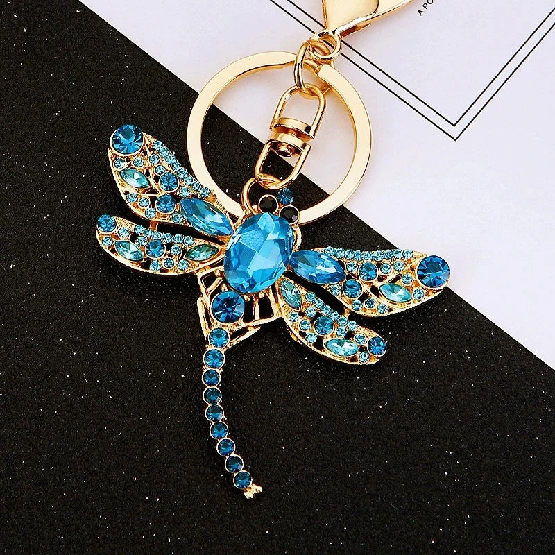 Gold-toned crystal dragonfly keychain featuring blue and gold accents on a black background.