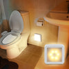 A motion sensor LED night light is mounted on a tiled wall next to a toilet in a bathroom setting.