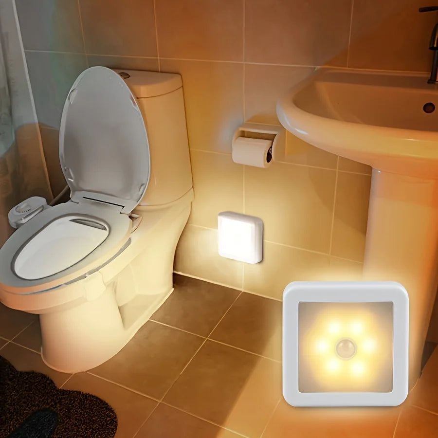 A motion sensor LED night light is mounted on a tiled wall next to a toilet in a bathroom setting.