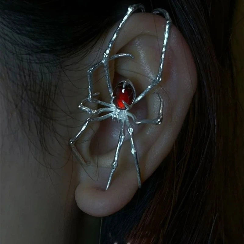 Silver spider ear cuff with a red gemstone detail worn on the ear.