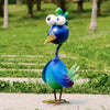 A blue metal peacock garden sculpture with large white eyes and a green crest standing on a path.