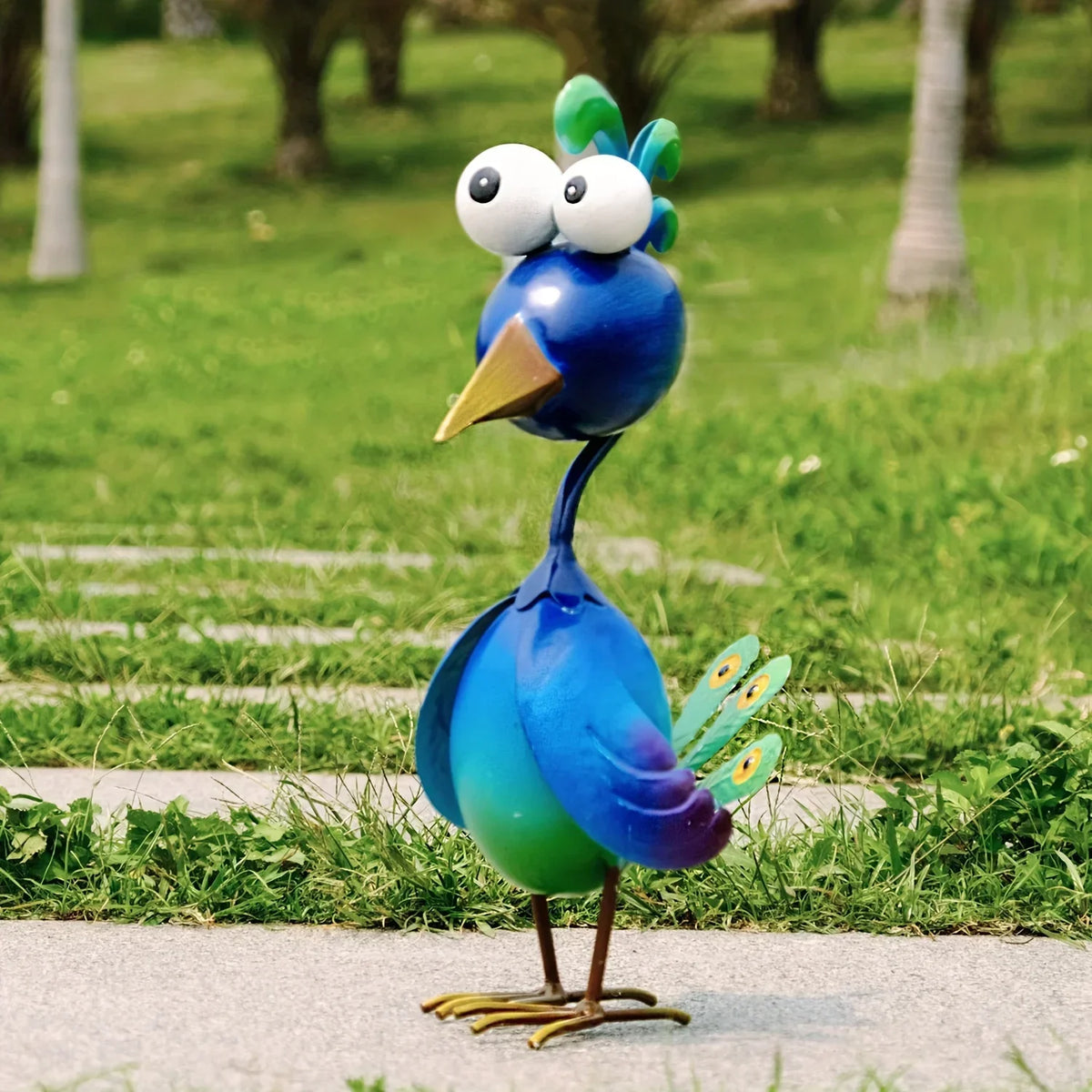 A blue metal peacock garden sculpture with large white eyes and a green crest standing on a path.