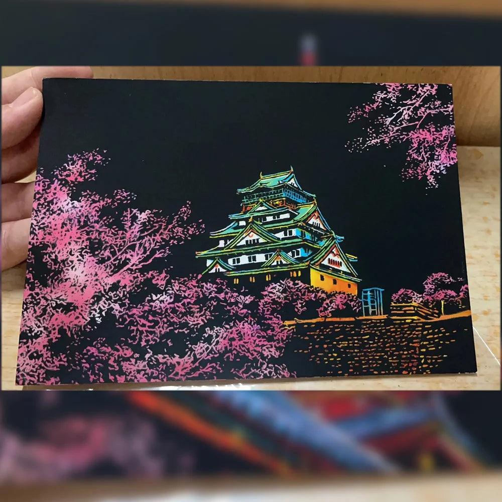 A DIY scratch painting art kit featuring a vibrant pink and green depiction of a traditional Japanese temple on a black backg