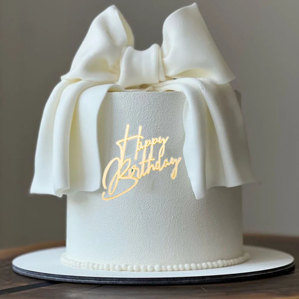 Weißer Geburtstagskuchen mit durchscheinendem Schleifenband und goldenem Schriftzug „Happy Birthday“