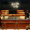 A bar counter with a wooden top and bar stools in a dimly lit interior featuring a neon sign that reads Good Vibes Only