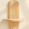 A vertical wooden wall shelf with concentric, parallel grooves mounted on a light-colored wall.