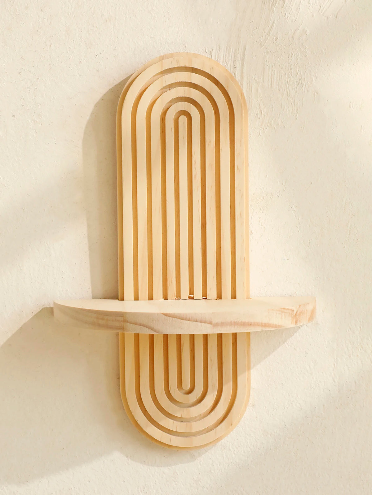 A vertical wooden wall shelf with concentric, parallel grooves mounted on a light-colored wall.