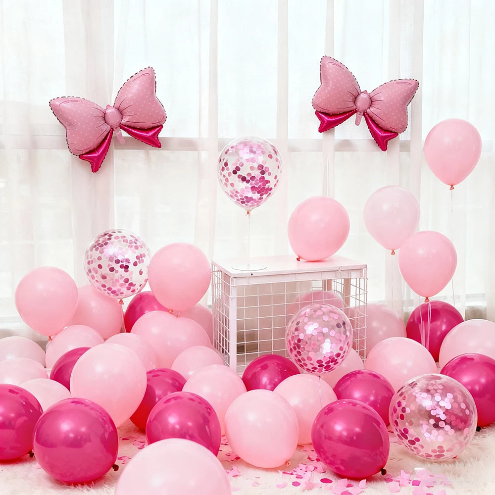 A collection of pink foil bow balloons in various shades of pink and magenta arranged on a white surface.